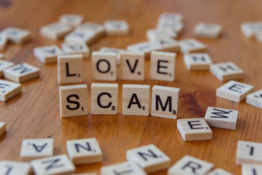 Scrabble tiles form words 'LOVE' and 'SCAM' on a wooden surface, illustrating deceit in relationships.