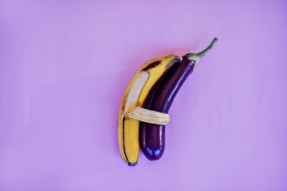 A vibrant and artistic arrangement of a banana and eggplant against a violet backdrop, highlighting color and freshness.