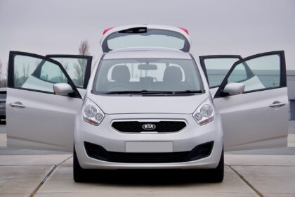 Front view of a silver Kia car with all doors open, parked on pavement.