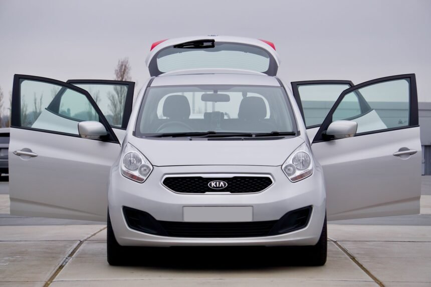 Front view of a silver Kia car with all doors open, parked on pavement.