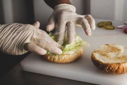 Close-up of a chef's hands in gloves preparing a sandwich in a kitchen setting.
