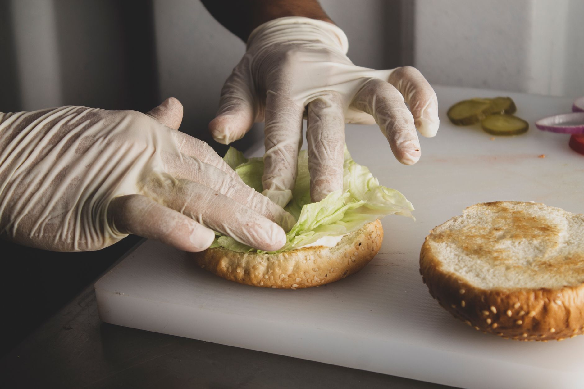 Close-up of a chef's hands in gloves preparing a sandwich in a kitchen setting.