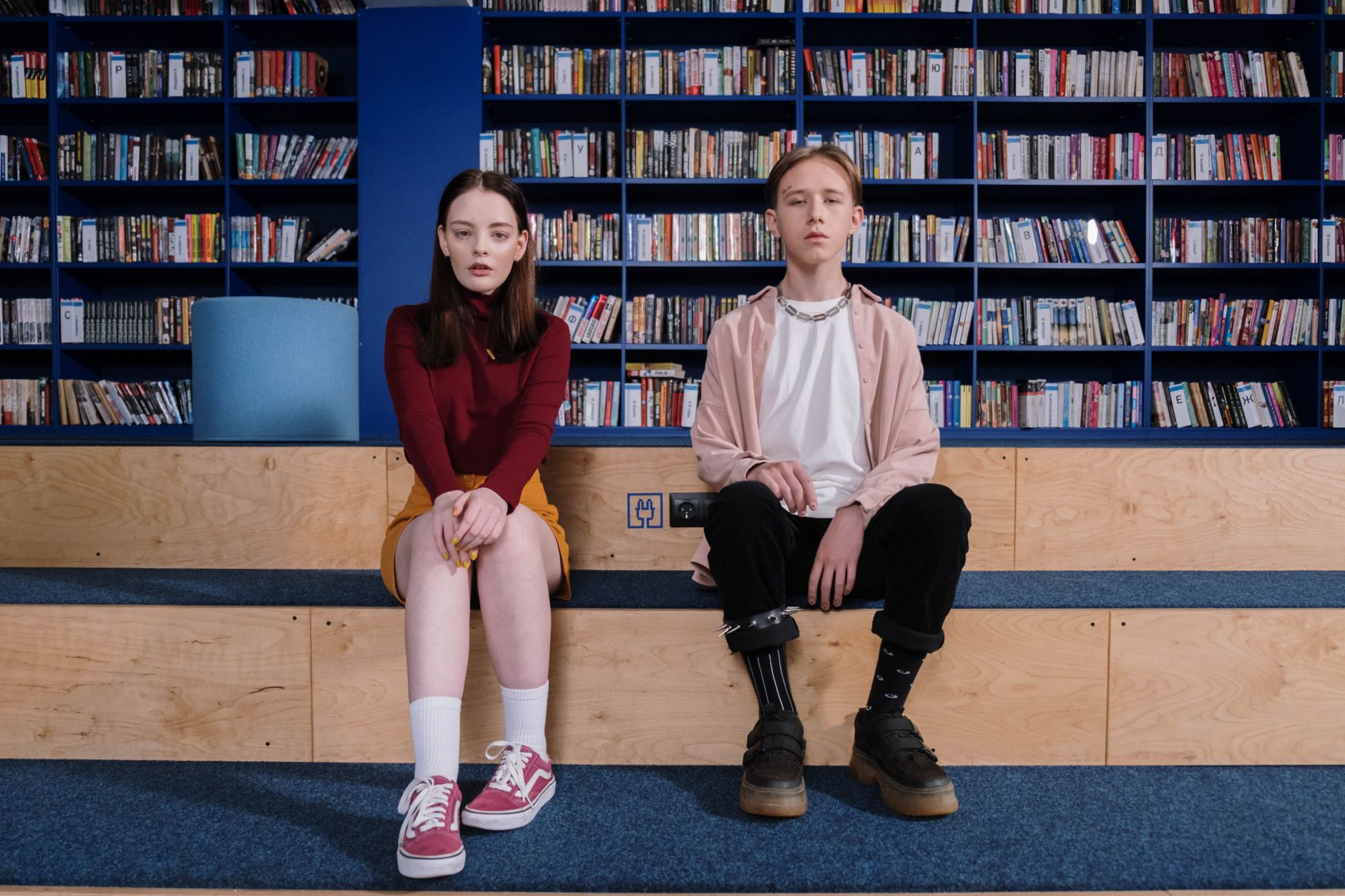 Two teenagers sitting on library steps, showcasing a modern casual fashion scene.