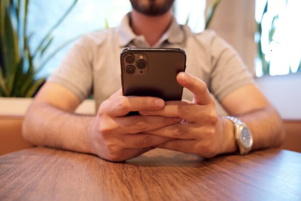 Close-up of a man holding a smartphone at a cafe table. Casual setting with plants in the background.