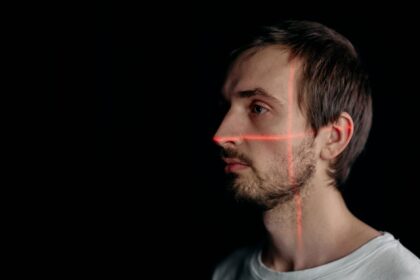 A side profile of a man with facial recognition laser scan on his face against a black background.