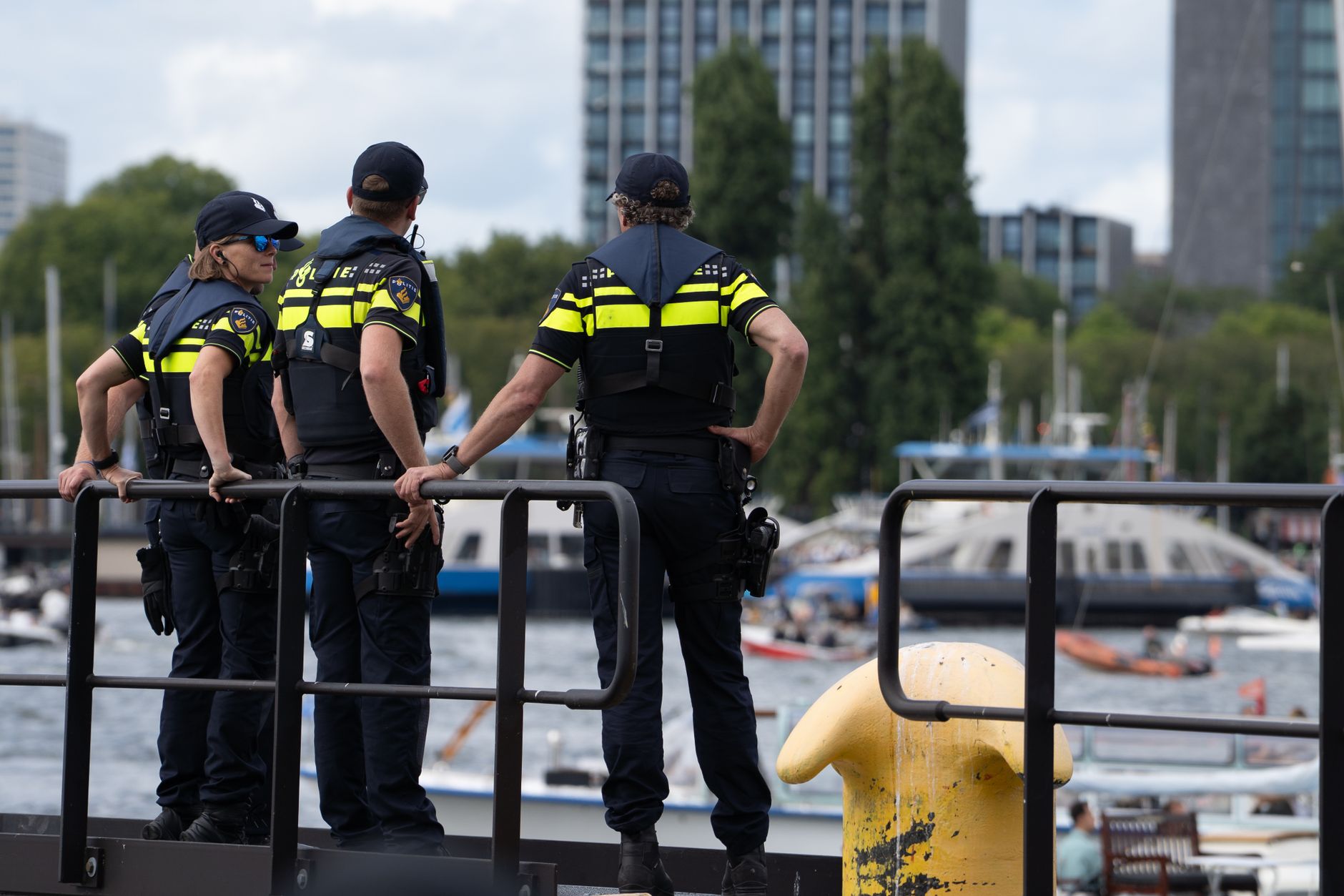 Police officers overlooking a vibrant waterfront area, with boats and cityscape in view.