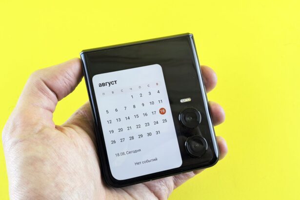 Close-up of a hand holding a flip smartphone with a calendar on screen against a vibrant yellow background.