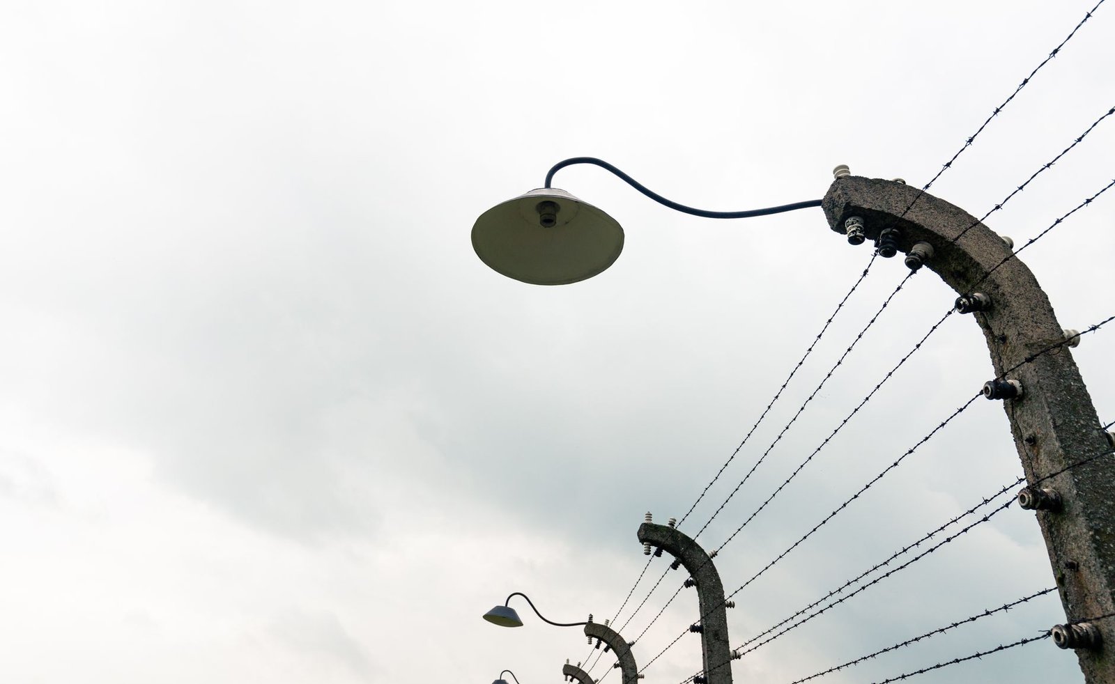 Low angle view of an overcast sky with barbed wire fence and lamps.