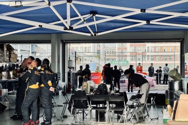A racing team preps in a pit garage while cars zoom past outside, highlighting teamwork and focus.