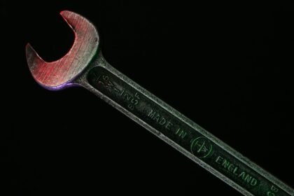 Close-up of a rusty wrench with a red hue on a dark background.
