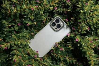 A smartphone surrounded by lush green leaves and small pink flowers, captured outdoors.