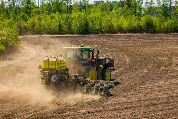 A tractor tills a vast field in rural North Carolina, surrounded by dense greenery.