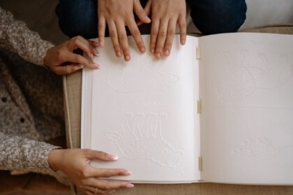 Adult and child hands exploring a tactile braille book with embossed animal illustrations.