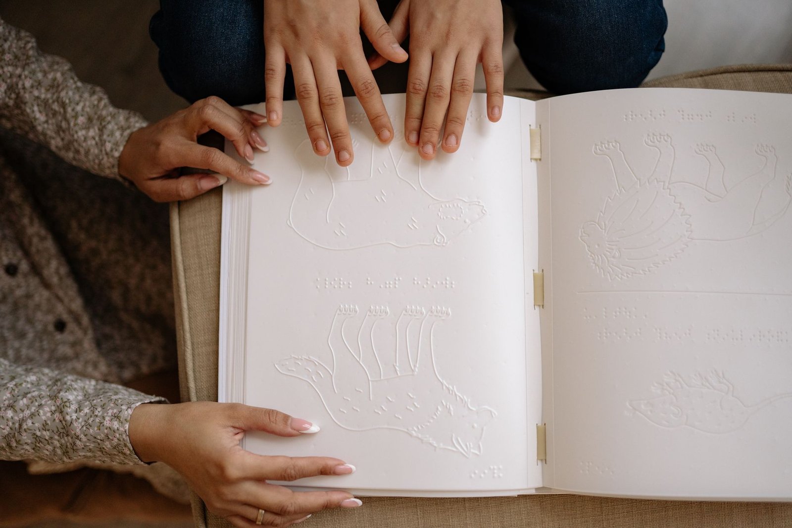 Adult and child hands exploring a tactile braille book with embossed animal illustrations.