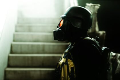 Dark indoor scene featuring a figure in gas mask and helmet, evoking horror and Halloween vibes.