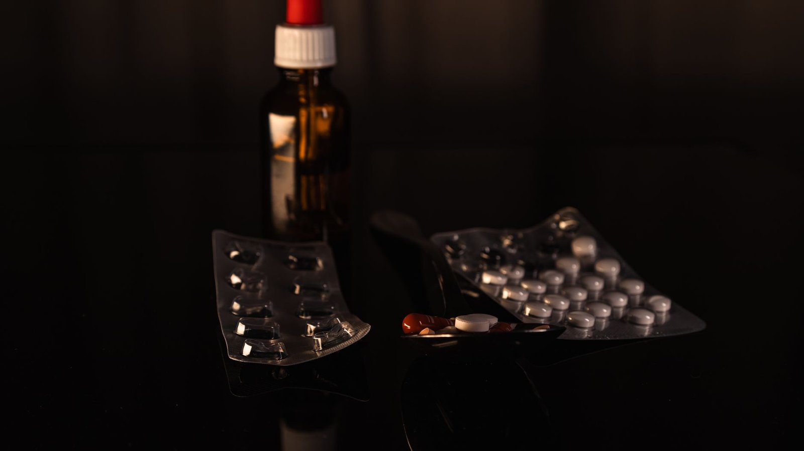 A collection of pharmaceuticals including pills and a bottle on a dark surface.