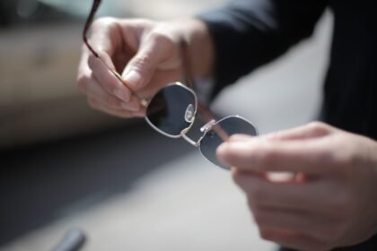 A detailed close-up of hands holding stylish sunglasses outdoors with a blurred background.