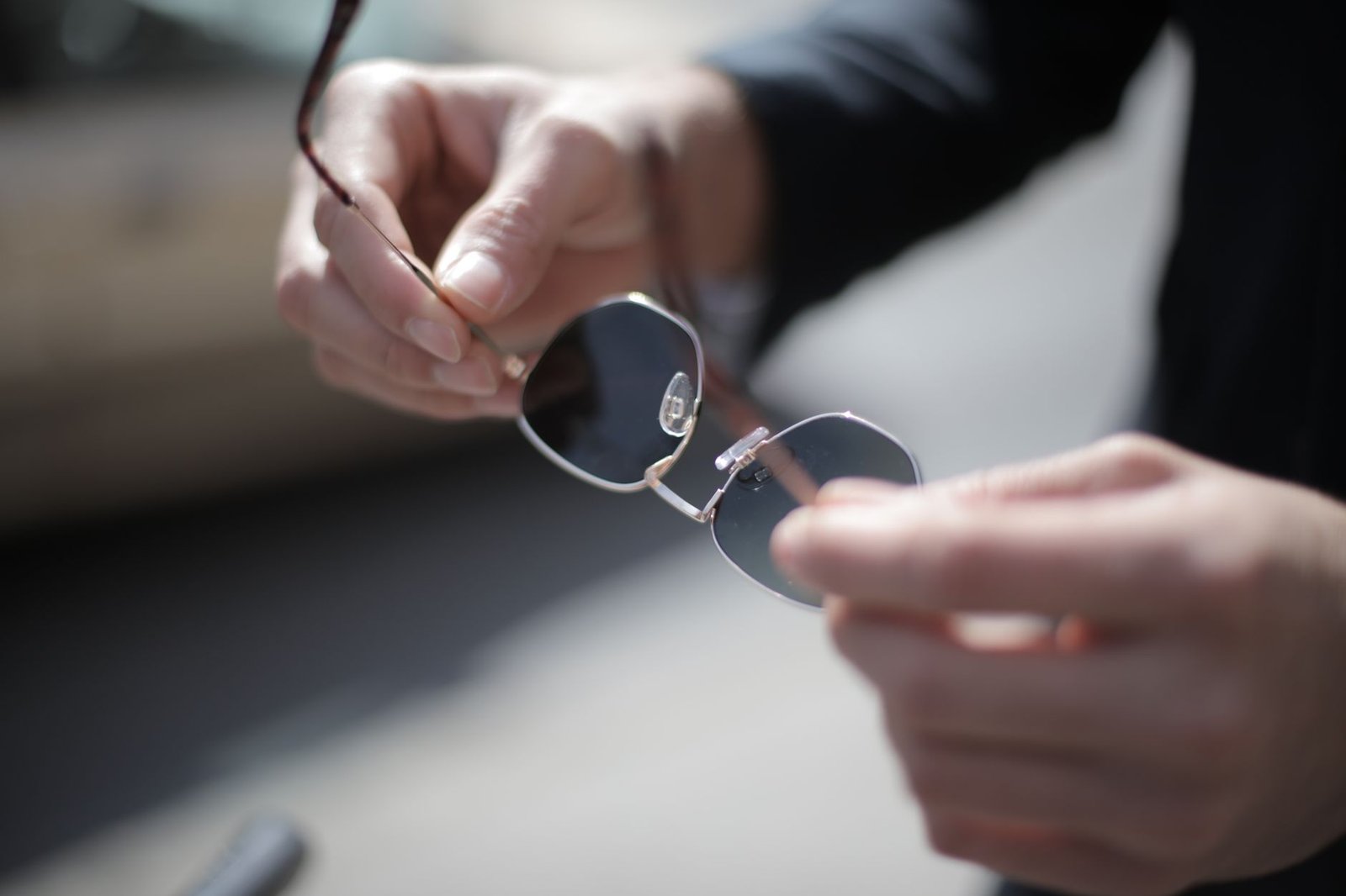 A detailed close-up of hands holding stylish sunglasses outdoors with a blurred background.