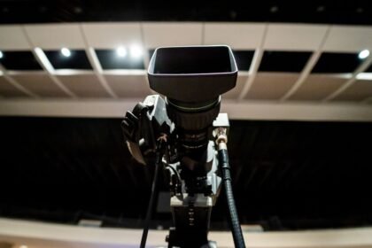 Low angle of professional video camera with lens on tripod placed under ceiling with lights in studio