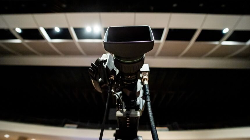Low angle of professional video camera with lens on tripod placed under ceiling with lights in studio