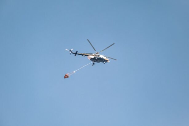 Helicopter with water bucket fighting a wildfire under a clear blue sky.