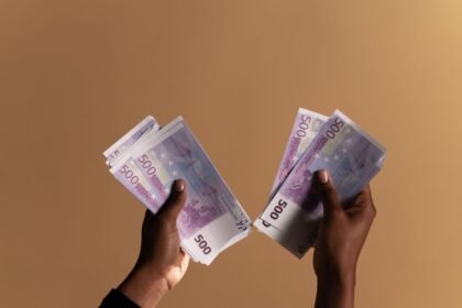 Close-up image of hands holding 500 euro banknotes on a neutral beige background.