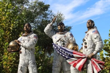 Bronze statue of Apollo astronauts at Cape Canaveral, holding a flag.