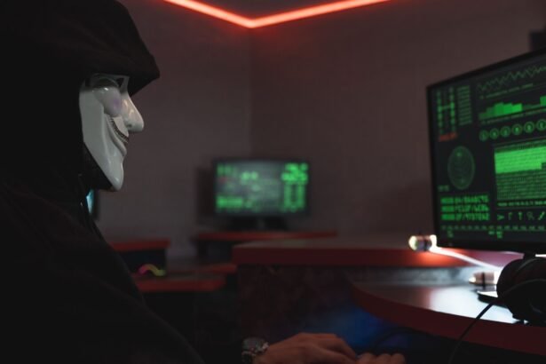 A person wearing a hacker mask operates a computer in a dimly lit room with digital displays.