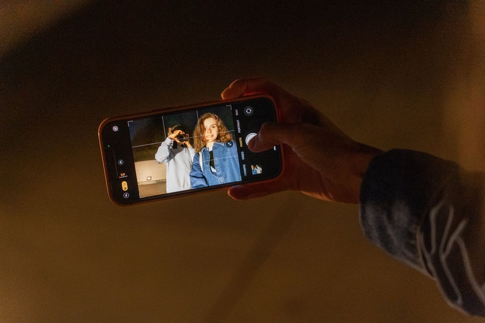 A couple capturing a romantic memory using a smartphone camera during nighttime indoors.