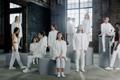 Diverse group of models in white outfits posing in an industrial setting, showcasing modern fashion.
