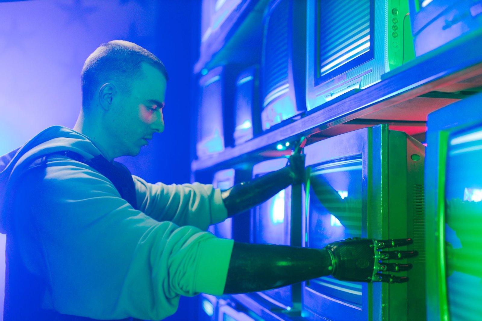 Man with prosthetic arms interacting with stack of CRT televisions, showcasing technology.