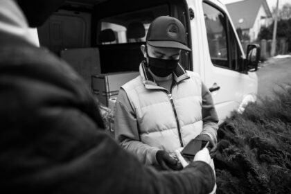 Courier in mask accepts contactless payment outside. Safe delivery concept.