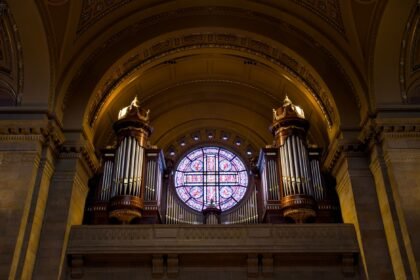 Ornate pipe organ and stained glass window inside a grand church interior, showcasing architectural elegance.