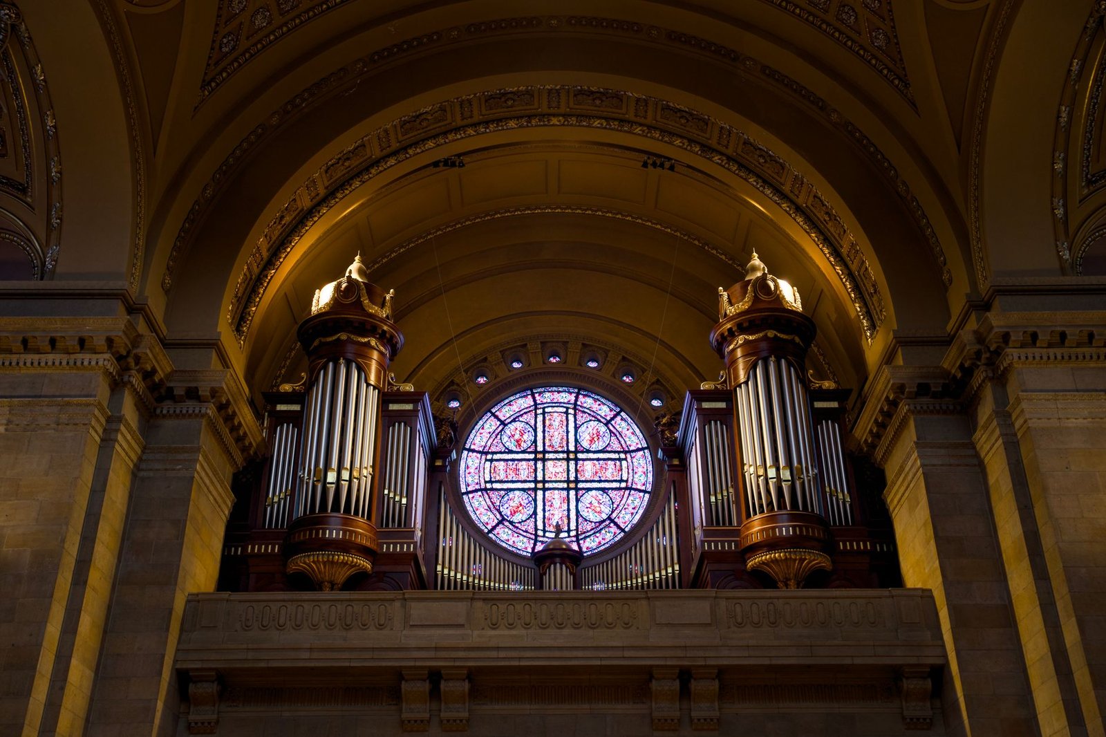 Ornate pipe organ and stained glass window inside a grand church interior, showcasing architectural elegance.