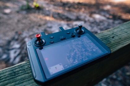 Close-up of a drone controller with visible screen, resting on a wooden surface outdoors.