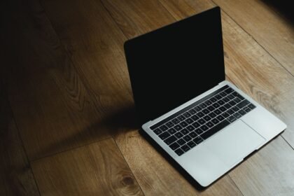 MacBook placed diagonally on a warm wooden floor with soft lighting.