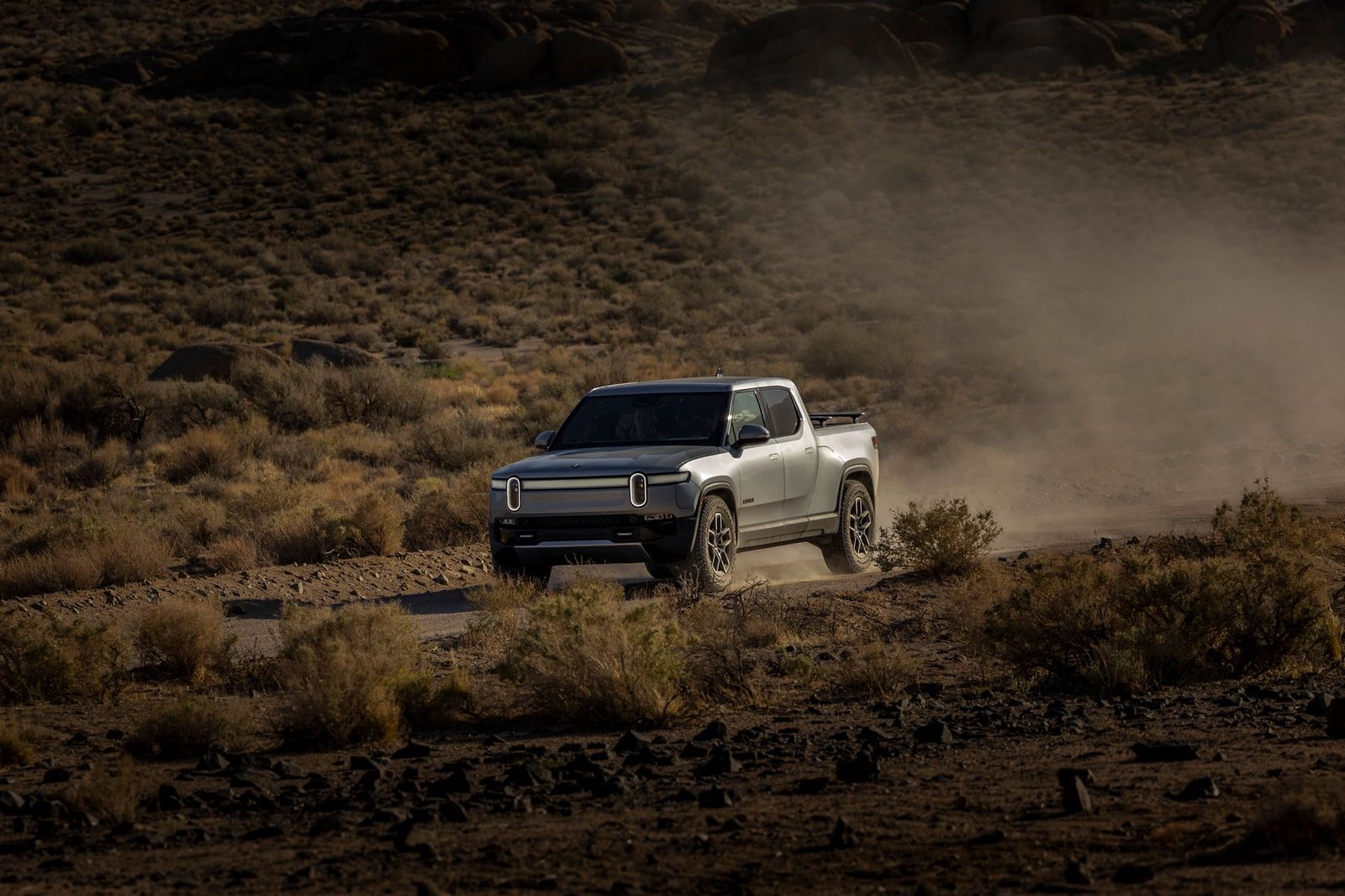 Modern electric truck navigating rugged desert terrain, raising dust clouds.