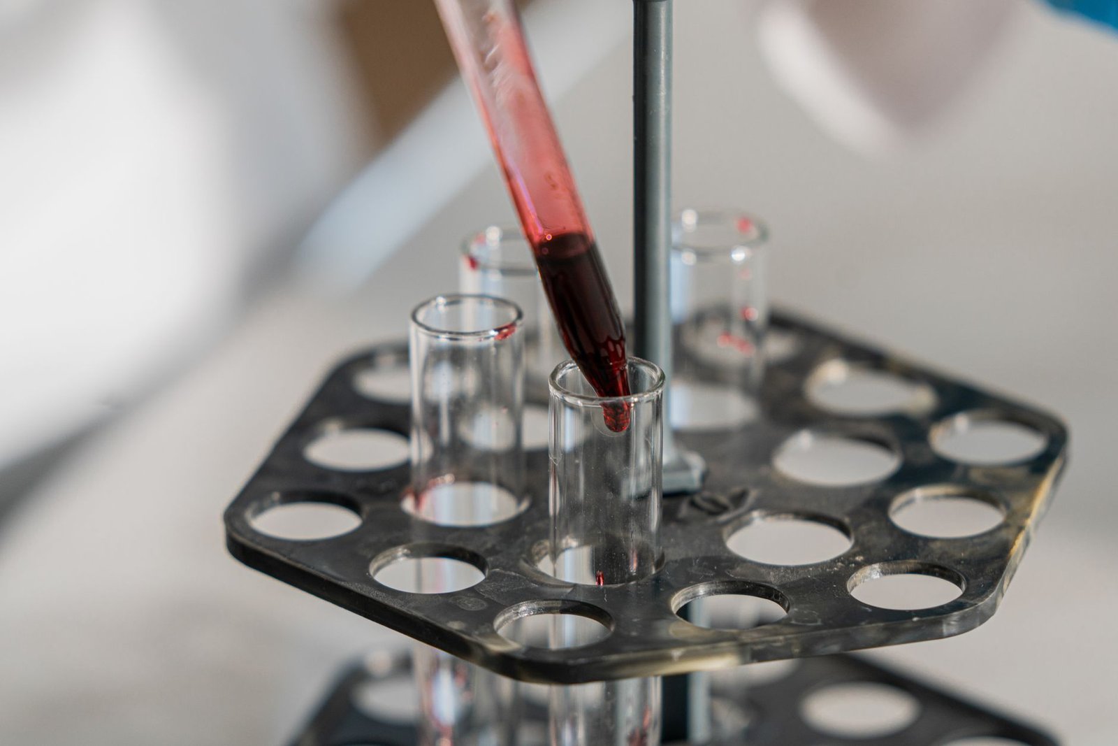 Red liquid being transferred into test tubes in a lab setting for research.
