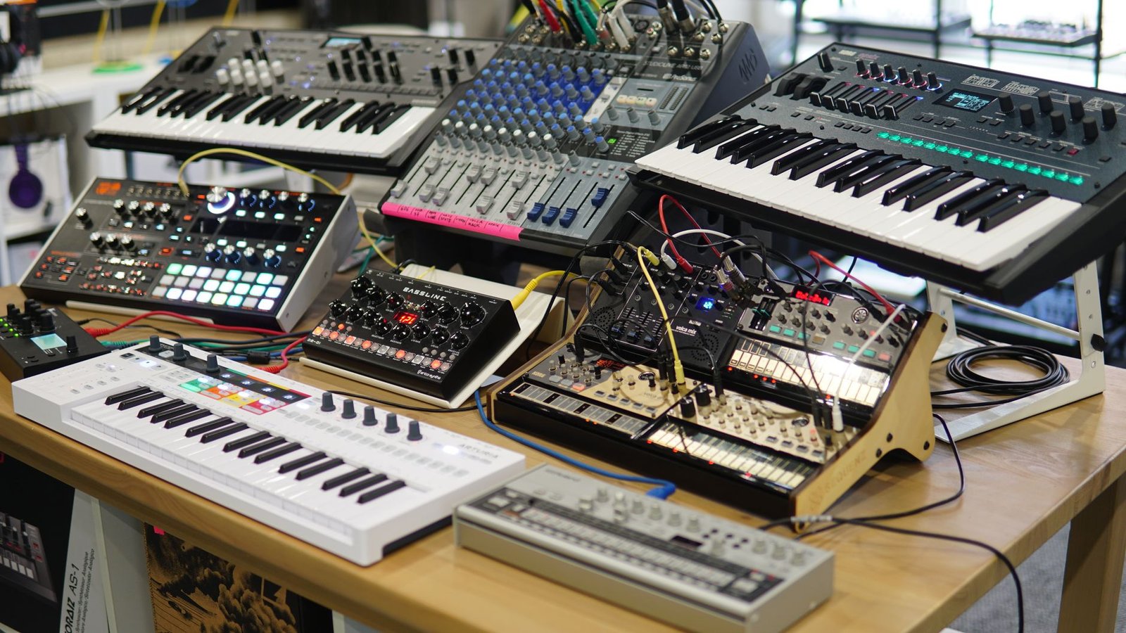 A diverse setup of electronic music production equipment on a wooden table, featuring synthesizers and sound mixers.