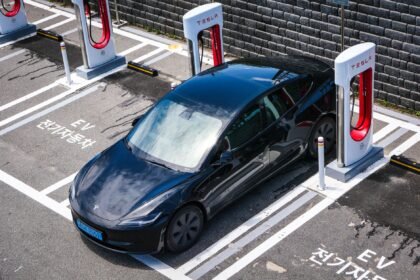 A black Tesla parked at a charging station in an urban setting.