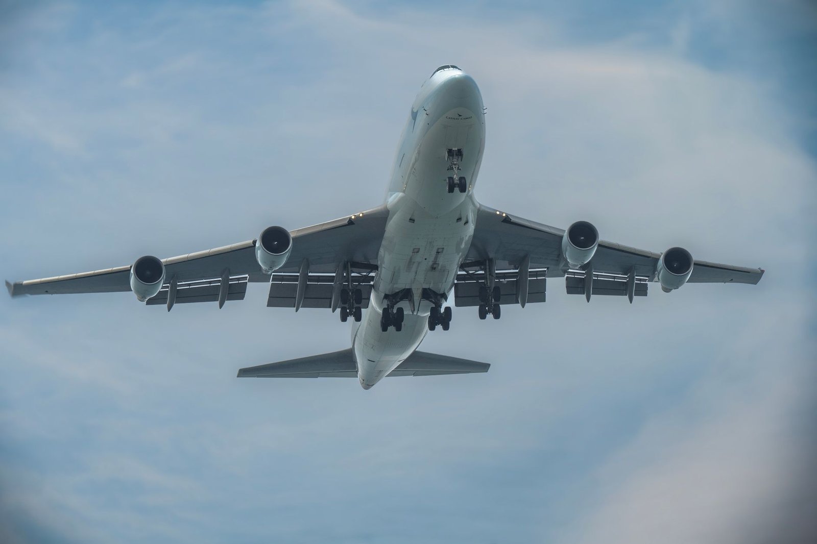 Airplane captured in-flight from below with landing gear down, set against a clear blue sky.