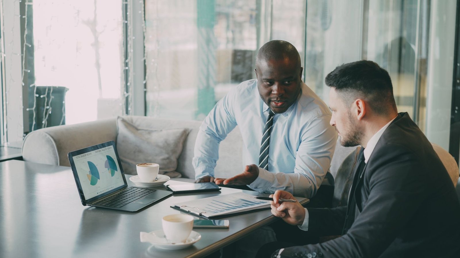 Two businessmen discussing data at a cafe while enjoying coffee.